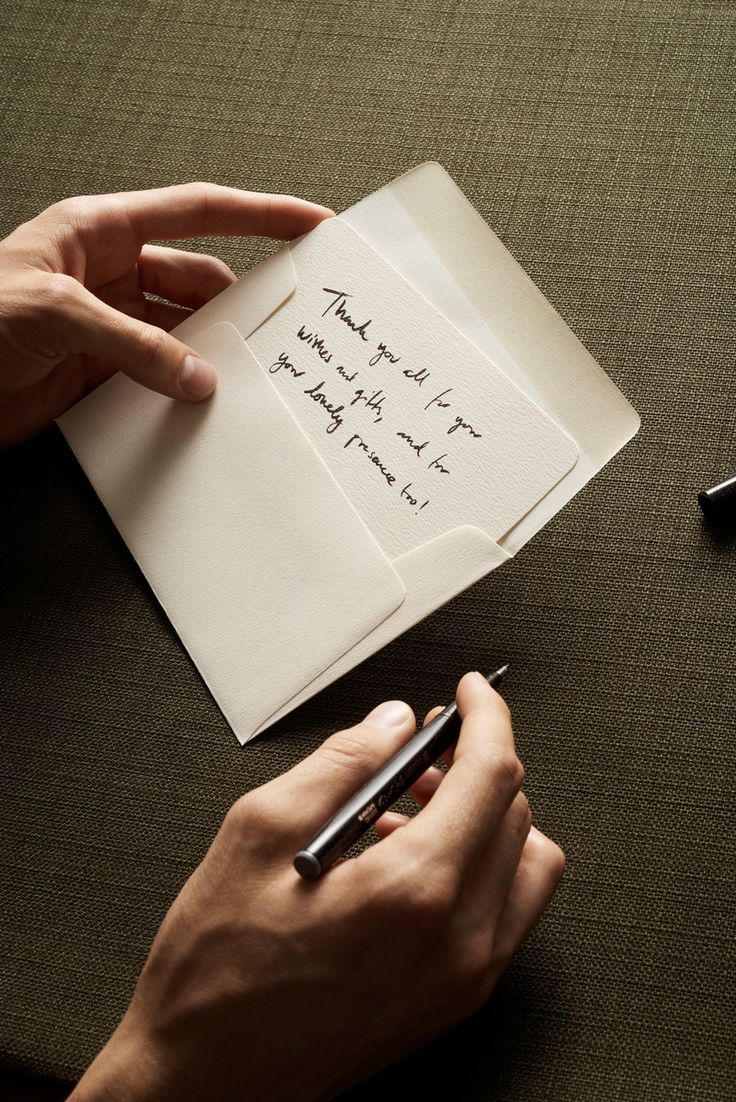 Hands writing a handwritten thank-you note on cream paper with a pen