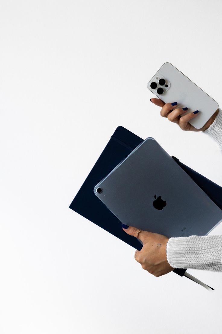 Hands holding an iPhone and a navy iPad against a white background